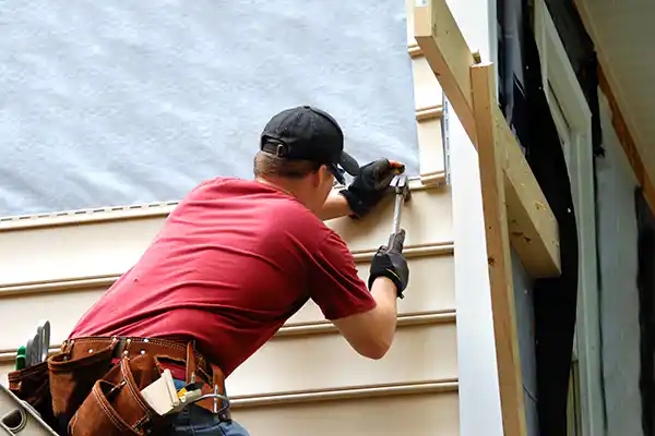 Worker installing new tan siding on a home with a hammer
